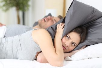 woman covers her head with a pillow because a man snores